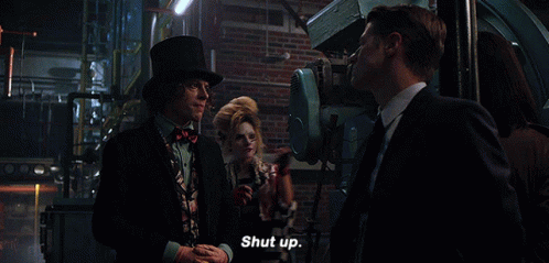 A Man In A Top Hat Says Shut Up In Front Of A Woman In A Striped Jacket GIF