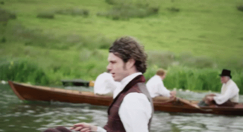 A Man In A Top Hat Sits In A Boat On A Lake GIF