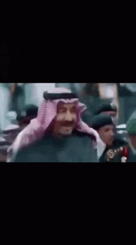A Man In A Traditional Arabic Costume Is Standing In Front Of A Crowd Of People . GIF
