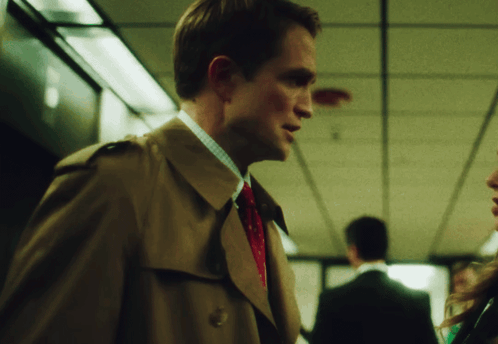 A Man In A Trench Coat And Tie Is Talking To Another Man GIF