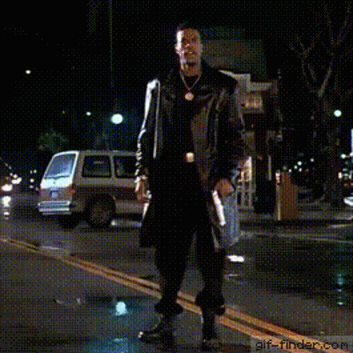 A Man In A Trench Coat Is Walking Down A Street At Night With His Arms Outstretched .. GIF