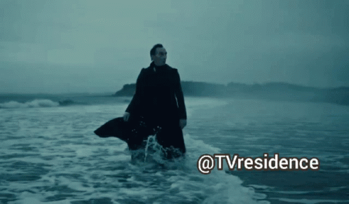 A Man In A Trench Coat Is Walking In The Ocean With The Words @Tvresidence Above Him GIF