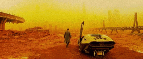 A Man In A Trench Coat Is Walking Towards A Car With Its Door Open In The Desert . GIF
