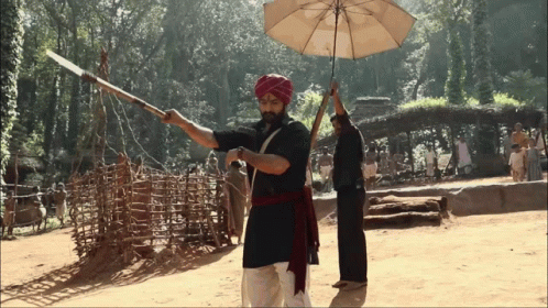 A Man In A Turban Is Holding An Umbrella And A Spear GIF