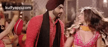 a man in a turban is standing next to a woman in a pink dress and talking to her .
