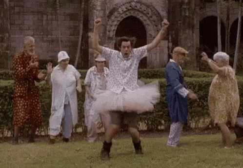 A Man In A Tutu Is Dancing With A Group Of Elderly People In A Park . GIF