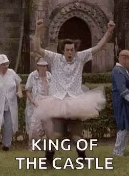A Man In A Tutu Is Jumping In The Air In Front Of A Castle . GIF