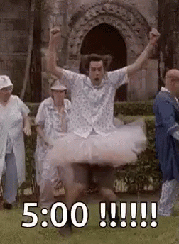 A Man In A Tutu Is Jumping In The Air While A Group Of People Watch . GIF