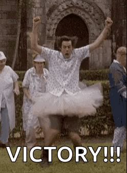 A Man In A Tutu Is Jumping In The Air With His Arms In The Air In Front Of A Group Of People . GIF