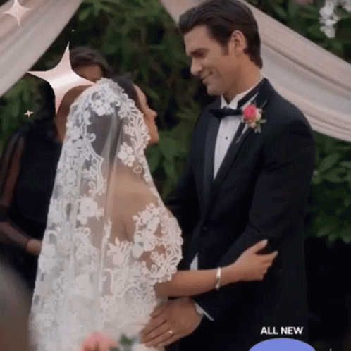 A Man In A Tuxedo And A Bride In A Wedding Dress Are Hugging GIF