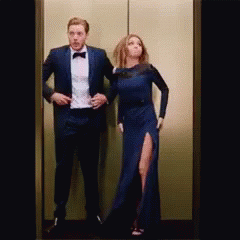 A Man In A Tuxedo And A Woman In A Dress Are In An Elevator . GIF