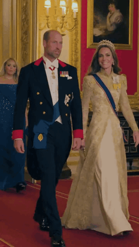 A Man In A Tuxedo And A Woman In A Gown Are Walking Down A Red Carpet GIF