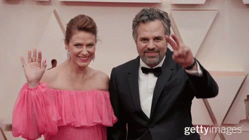 A Man In A Tuxedo And A Woman In A Pink Dress Are Standing Next To Each Other GIF