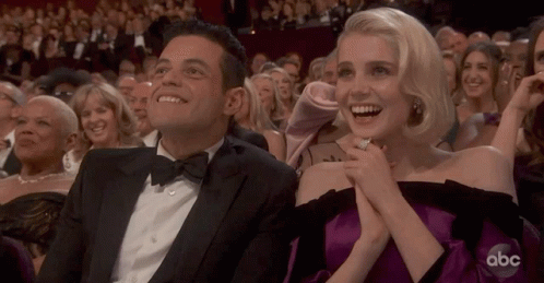 A Man In A Tuxedo And A Woman In A Purple Dress Are Sitting In The Audience At An Abc Awards Show GIF