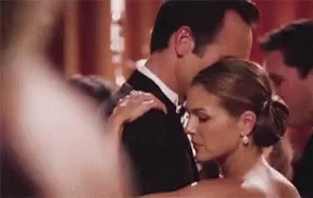 A Man In A Tuxedo And A Woman In A White Dress Are Dancing Together . GIF