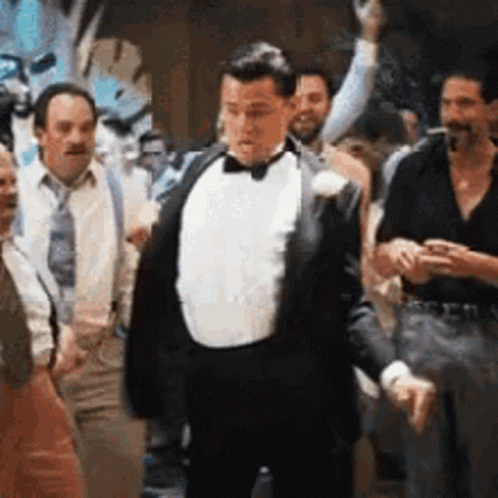 A Man In A Tuxedo And Bow Tie Is Dancing In A Crowd Of People . GIF