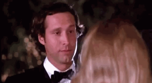 A Man In A Tuxedo And Bow Tie Is Looking At A Woman In A Red Dress . GIF