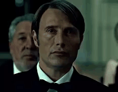 A Man In A Tuxedo And Bow Tie Is Looking At The Camera With Two Men Behind Him . GIF