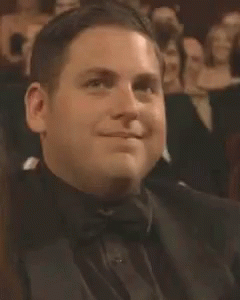 A Man In A Tuxedo And Bow Tie Is Smiling While Sitting In A Theatre . GIF