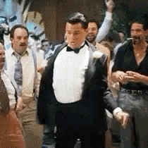 A Man In A Tuxedo And Bow Tie Is Standing In A Crowd Of Men . GIF