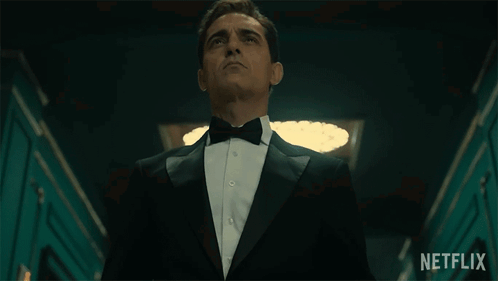 A Man In A Tuxedo And Bow Tie Is Standing In A Hallway With A Netflix Logo In The Background GIF