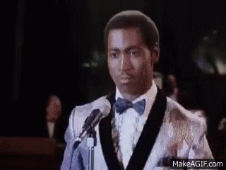 A Man In A Tuxedo And Bow Tie Is Standing In Front Of A Crowd Of People . GIF