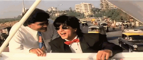 A Man In A Tuxedo And Bow Tie Is Talking To Another Man GIF