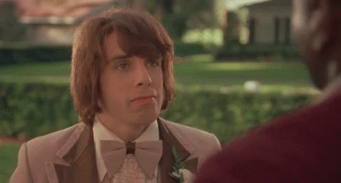 A Man In A Tuxedo And Bow Tie Is Talking To Another Man In A Park . GIF