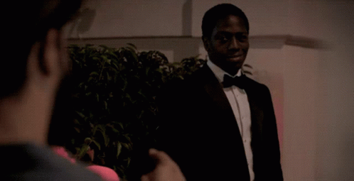 A Man In A Tuxedo And Bow Tie Is Talking To Another Man GIF