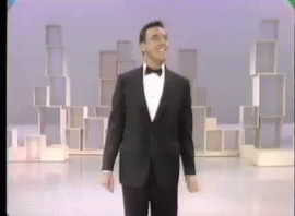 A Man In A Tuxedo And Bow Tie Is Walking On A Stage GIF