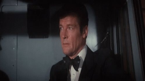 A Man In A Tuxedo And Bow Tie Looks Out Of A Window GIF