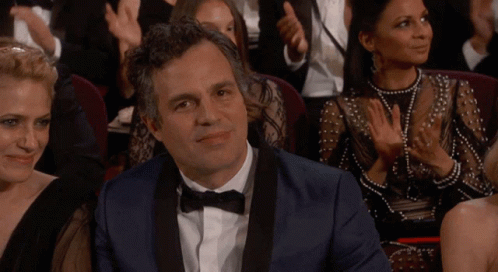 A Man In A Tuxedo And Bow Tie Sits In A Theatre Applauding GIF