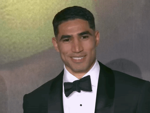 a man in a tuxedo and bow tie smiles at the camera