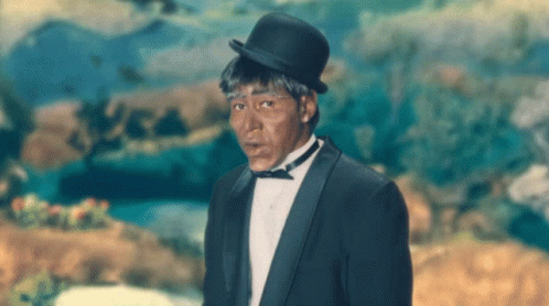 A Man In A Tuxedo And Bowler Hat Is Standing In Front Of A Painting GIF