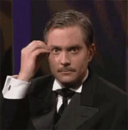A Man In A Tuxedo And Tie Is Scratching His Forehead . GIF