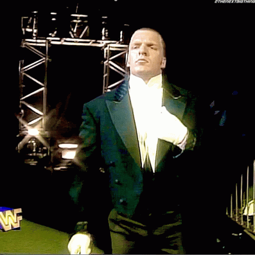 A Man In A Tuxedo And White Gloves Stands In Front Of A Wwe Logo GIF
