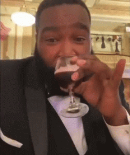 A Man In A Tuxedo Drinking A Glass Of Wine GIF