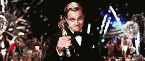 A Man In A Tuxedo Holding An Oscar Statue GIF