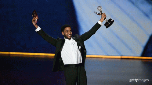 A Man In A Tuxedo Holds A Trophy In His Hands GIF