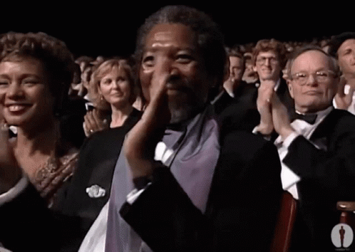 A Man In A Tuxedo Is Applauding In Front Of A Crowd GIF
