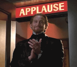 A Man In A Tuxedo Is Clapping In Front Of A Sign That Says Applause GIF