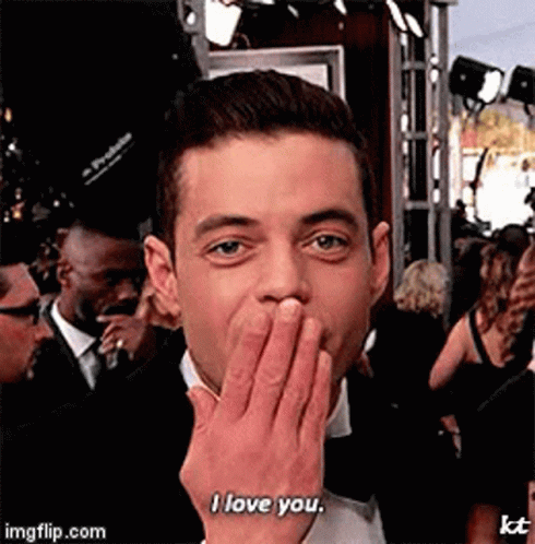 A Man In A Tuxedo Is Covering His Mouth With His Hand And Saying I Love You . GIF
