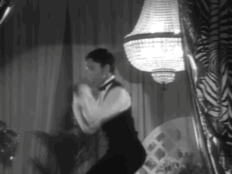 A Man In A Tuxedo Is Dancing In A Black And White Photo GIF