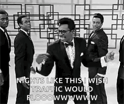 A Man In A Tuxedo Is Dancing In Front Of A Group Of Men . GIF