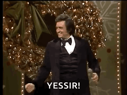A Man In A Tuxedo Is Dancing On A Stage In Front Of A Christmas Tree While Holding A Microphone . GIF