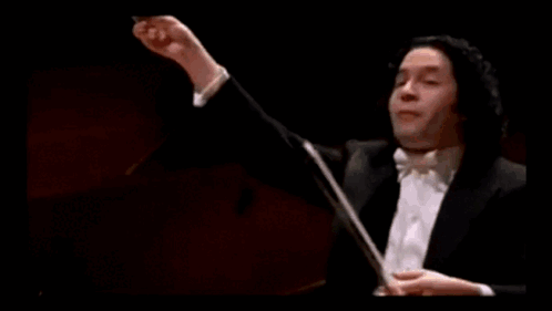 A Man In A Tuxedo Is Holding A Baton In Front Of A Green Bar With A Gold Coin On It GIF
