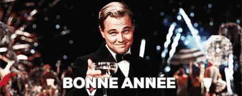 A Man In A Tuxedo Is Holding A Glass Of Wine In Front Of A Sign That Says Bonne Année GIF