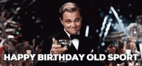 A Man In A Tuxedo Is Holding A Glass Of Wine In His Hand And Says Happy Birthday Old Sport . GIF