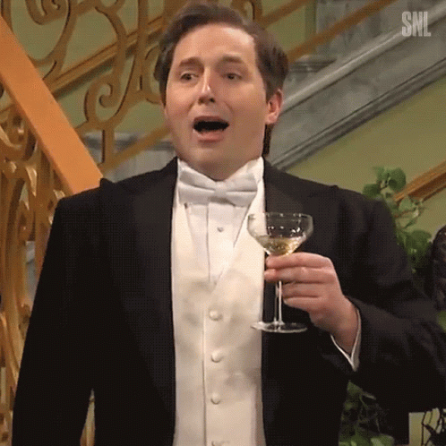 A Man In A Tuxedo Is Holding A Glass Of Wine In His Hand . GIF