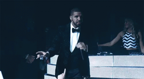 A Man In A Tuxedo Is Holding A Microphone In Front Of A Crowd GIF